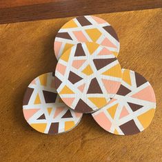 three coasters are sitting on top of a wooden table, each with different colored geometric designs