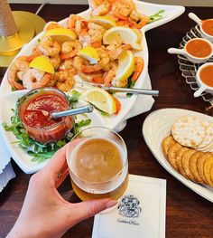 a person holding a beer in front of a platter of shrimp and crackers