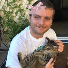 a man holding a cat with a pink bow on it's head and smiling at the camera