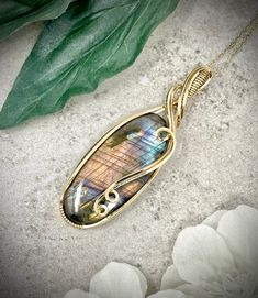 This pendant features a gorgeous, huge oval shaped spectrolite cabochon wrapped in 14k gold filled wire.  Spectrolie is gem-grade labradorite and usually contains rarer flash colors such as gold, purple, pink, and orange.  This spectrolite contains pretty much the entire spectrum of available flash colors for labradorite: blue, gold, orange, purple, and pink.   About the Pendant: - Non-tarnish - Safe for folks with metal sensitivities and allergies  - Safe for daily wear; wont damage with friction, polishing, etc.   - Has an expected lifespan similar to solid gold The pendant will be gift wrapped in a jewelry box with a complimentary 14k gold filled necklace (chain).  Care instructions will be included in your package as well as a polishing cloth to keep your silver bright and shiny.  This Wire Wrapped Cabochon, Wire Wrapped Crystal Pendant, Wire Wrap Cabochon, Jewelry Knowledge, Wire Wrap Jewelry Designs, Gold Filled Necklace, Labradorite Necklace, Handmade Wire Wrapped, Labradorite Necklaces