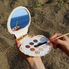 a person holding a mirror and brush in their hand with the ocean in the background