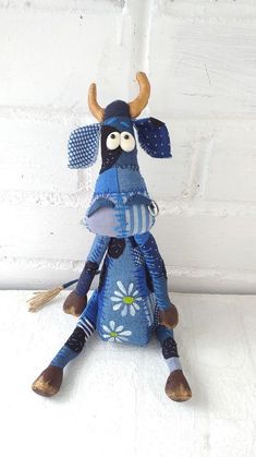 a blue stuffed animal with horns and polka dots on it's head sitting against a white brick wall