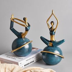 two figurines sitting on top of a book and one is holding a yoga pose