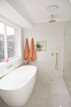 a white bath tub sitting under a window next to a shower head and two orange towels hanging on the wall