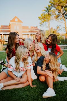 a group of young women sitting on top of a lush green field next to each other