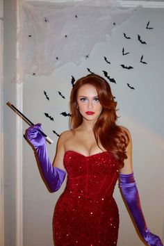 a woman in a red dress and purple gloves with bats on the wall behind her