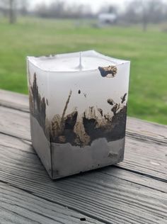 a square candle holder sitting on top of a wooden table next to a green field