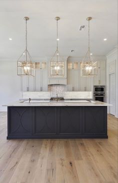 a large kitchen with an island in the middle and two chandeliers hanging from the ceiling