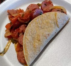 a taco with meat and vegetables on a white plate