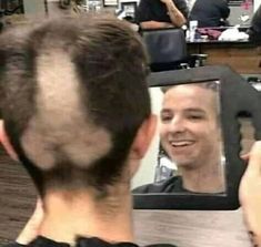 a man is looking at his reflection in the mirror while he shaves his hair