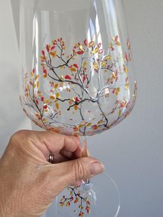 a hand holding up a wine glass with painted branches on the outside and yellow leaves on the inside