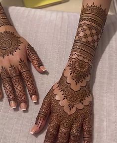 two hands with henna tattoos on them sitting on a bed next to each other