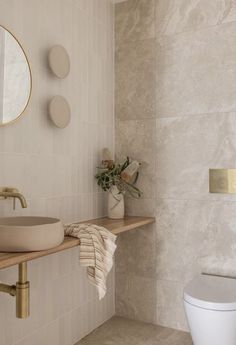 a white toilet sitting next to a sink in a bathroom under a round mirror on a wall