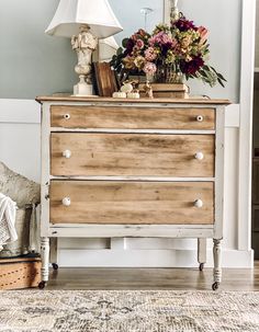 an old dresser with flowers on top in a room next to a lamp and bed