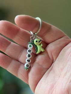 a hand holding a keychain with a small green dinosaur on it's side