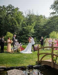 a bride and groom are kissing in front of their wedding party on the bridge over a pond