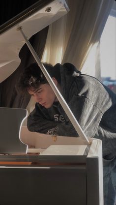 a young man playing the piano in front of a window