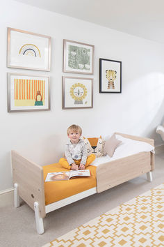 a little boy sitting on a bed with a book in his hand and some pictures above him