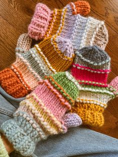 a pile of knitted mittens sitting on top of a wooden floor next to a person's leg