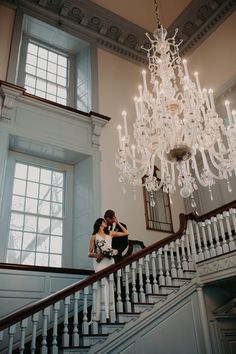 a bride and groom kissing under a chandelier at the top of some stairs