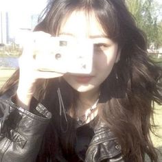 a young woman taking a selfie with her cell phone in the park while wearing a leather jacket