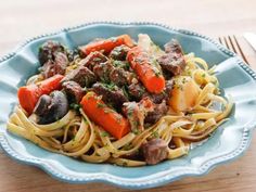 a blue bowl filled with pasta and meat on top of a wooden table next to a fork