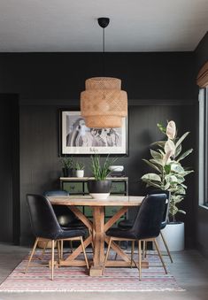 a dining room with black walls and wooden table surrounded by leather chairs, potted plants and framed pictures on the wall