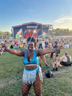 a woman in a blue top is dancing on the grass at an outdoor music festival