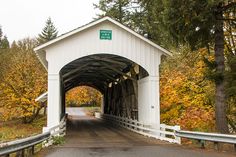 a white covered bridge in the fall with trees and leaves on both sides that are turning yellow