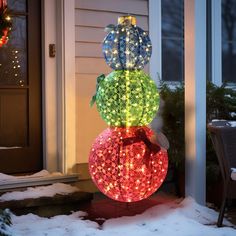 three balls with lights on them sitting in the snow next to a door and window