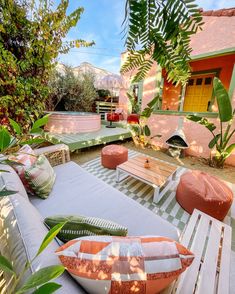 an outdoor seating area with cushions and pillows on the ground, surrounded by trees and plants