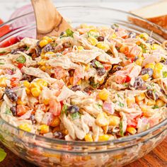 a salad with chicken, corn and tomatoes in a glass bowl on a wooden table