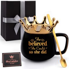 a black coffee mug with a gold crown on top and a gift box behind it