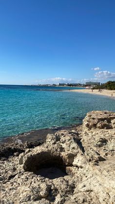 the beach is clear and blue with people walking on the rocks near it in front of the water