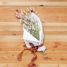 a bouquet of flowers wrapped in white paper on a wooden floor with brown ribbon around it