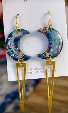 a pair of earrings that are hanging from a card with the moon and stars on it