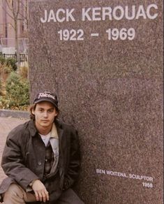 a young man sitting on the ground next to a stone wall with a name plaque