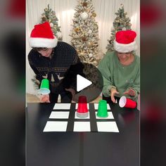 two people sitting at a table with christmas decorations on it and one person wearing a santa hat