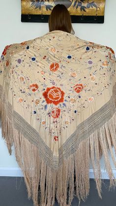 Here is a beautiful antique silk embroidered Manton de Manila shawl dating to the early part of the 20th century circa 1900 to 1910. The silk ground is in a rare buttermilk colour, I think that the listing photos which shows it worn by our model give a good indication of the actual colour. The richly coloured embroidery is in colours including orange, blue, lilac and white and it has long fringing and a hand knotted deep border to each side. The design includes large peony flowers and smaller fl 1920s Shawl, Blue Lilac, Peony Flowers, The 20th Century, Peony Flower, Embroidered Silk, Buttermilk, Shawls And Wraps, Manila