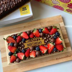 a birthday cake decorated with strawberries and chocolate on a cutting board next to a box of milk