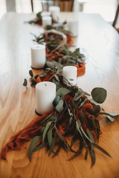 candles are lined up on the table with greenery