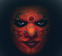 a woman's face painted in red and black with an elaborate mask on it