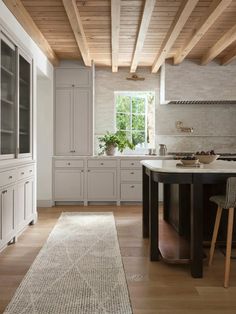 a large kitchen with white cabinets and wooden ceilinging, along with an area rug on the floor