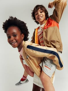 two young children posing for the camera with their arms around each other, both wearing jackets and shorts