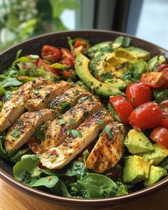 a salad with chicken, avocado and tomatoes in a bowl on a table