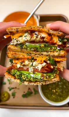 a hand holding a sandwich with cheese, lettuce and other toppings on it