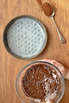 a person holding a whisk in a bowl next to a wooden table