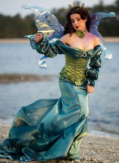 a woman in a green dress is standing on the beach with her arms out and wings outstretched