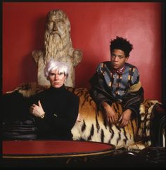 two people sitting on a tiger couch in front of a table with a statue behind them