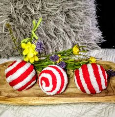 three red and white striped ball ornaments on a wooden platter with daffodils